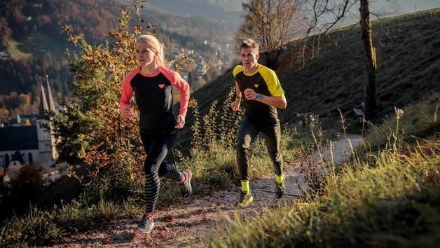 Zwei Läufer joggen im Herbstlicht auf einem schmalen Waldweg